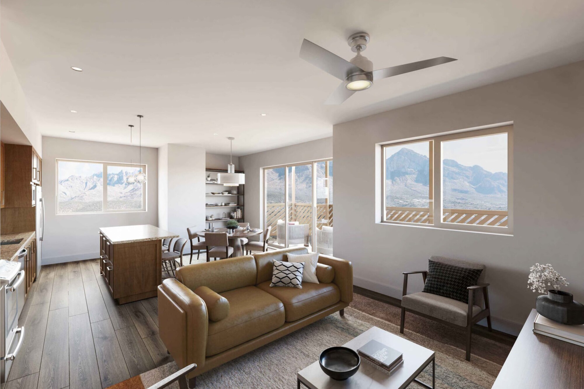 Bougainvillea A apartment interior showing an open living, dining and kitchen area with dark wood flooring and expansive mountain views. The living room includes a tan leather sofa, accent chairs and coffee table, while the kitchen has a center island and the dining area sits beside sliding doors leading to a private balcony.
