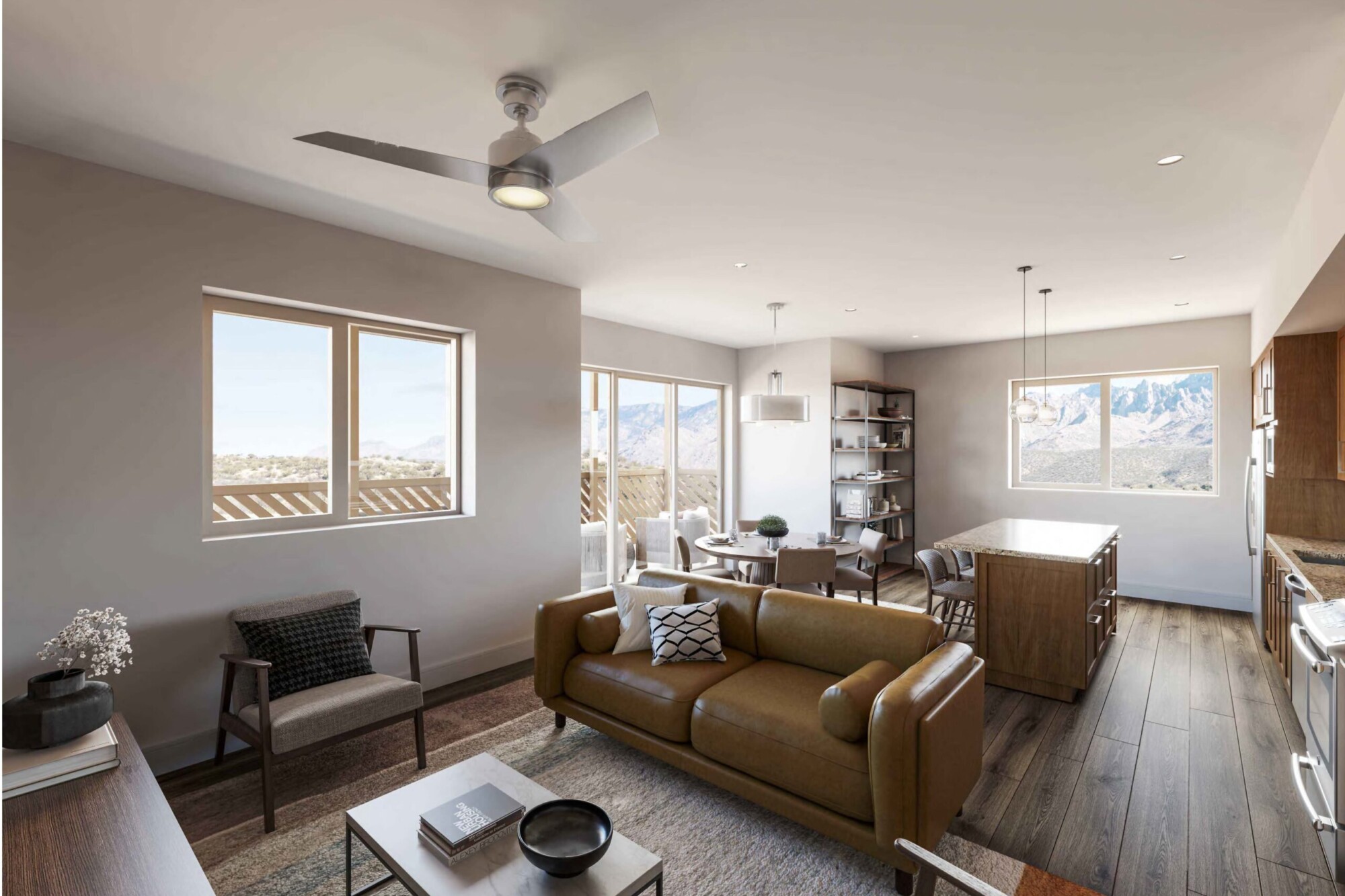 Bougainvillea B apartment living area featuring a tan leather sofa, accent chairs and coffee table in an open layout connected to the dining area and kitchen. Large windows and sliding glass doors overlook mountain scenery and provide access to a private balcony, while the kitchen includes a large center island.