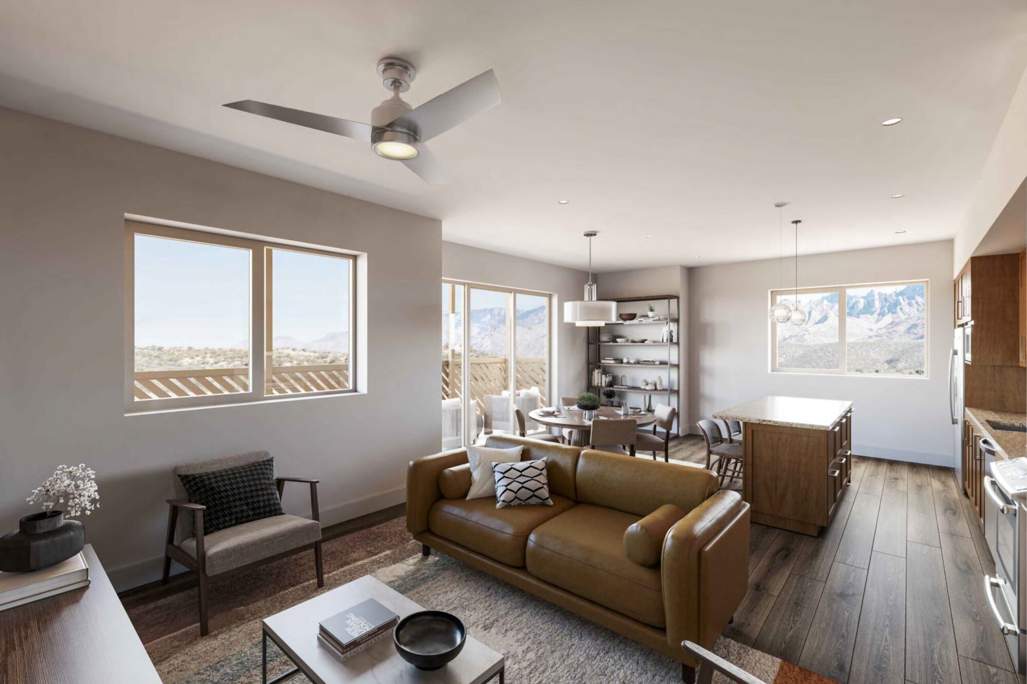 Bougainvillea C apartment interior showing a spacious open-concept living room, dining area and kitchen with dark wood flooring. Furnishings include a tan leather sofa, accent chairs and coffee table, with a kitchen island and dining table beyond. Large windows and balcony doors provide mountain views and natural light.