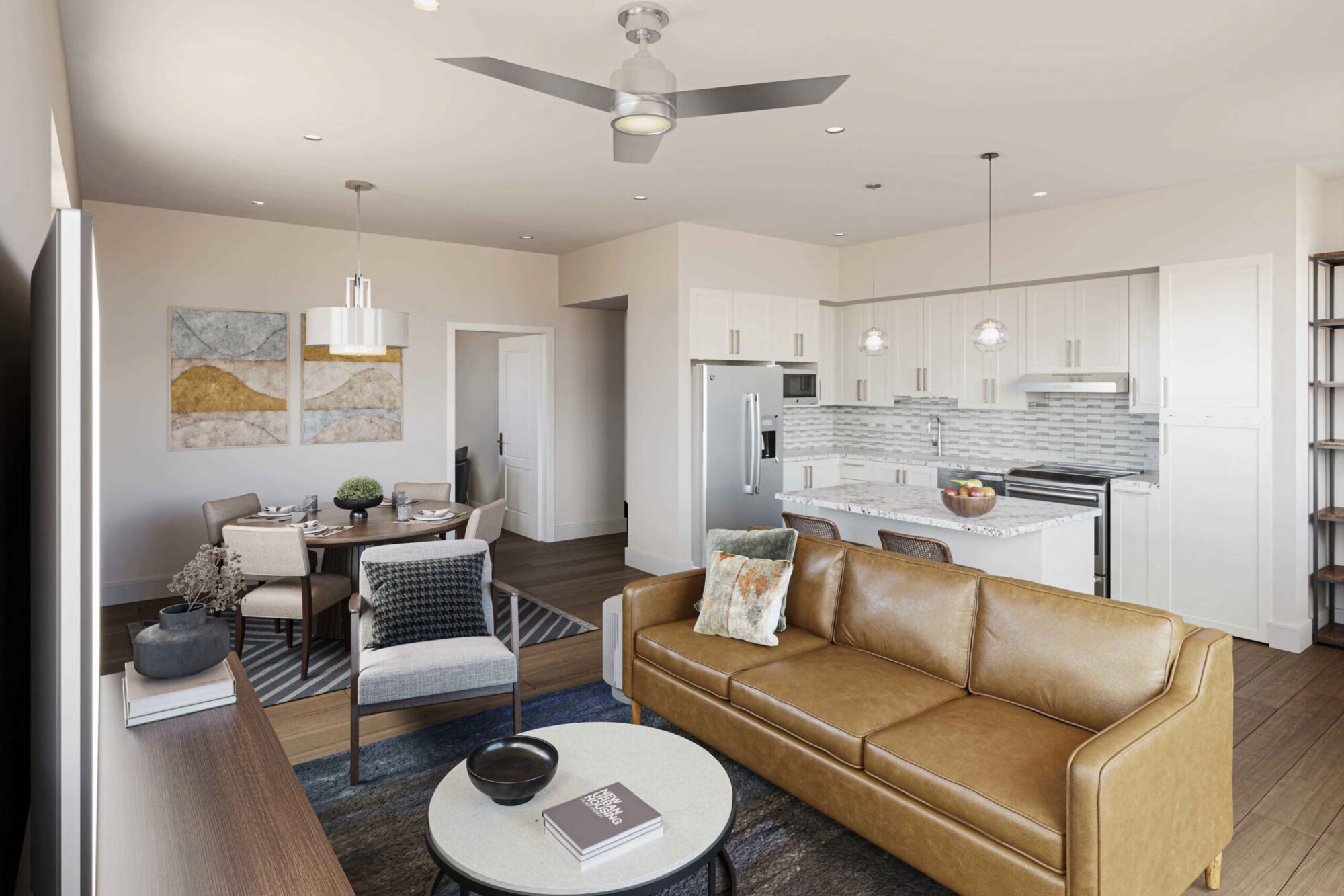 Honeysuckle B apartment interior showing an open-concept living room, dining area and kitchen with dark wood flooring. The living room includes a tan leather sofa, accent chair and round coffee table, while the kitchen features white cabinetry, stainless steel appliances, stone countertops, a tile backsplash and an island with bar seating.