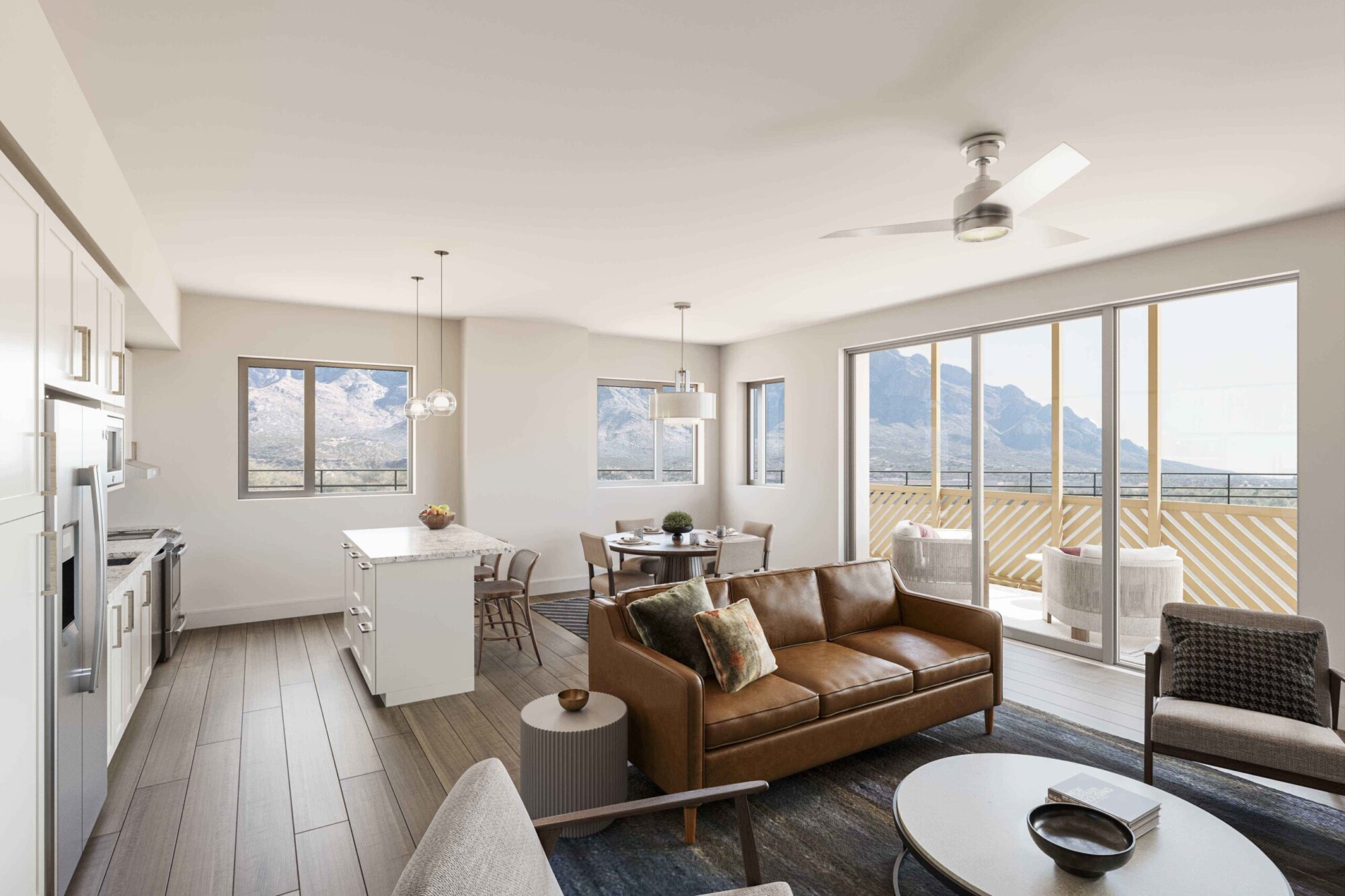 Verbena apartment interior featuring an open living, dining and kitchen layout with wood-look flooring, a brown leather sofa, accent chairs and round coffee table. The white kitchen includes a center island while expansive windows and sliding doors open to a furnished balcony with mountain views.